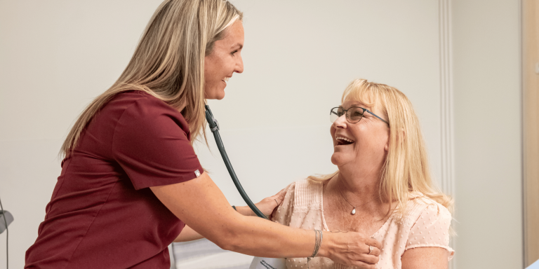 nurse in maroon scrubs holds a stethoscope to check a patients heartbeat.