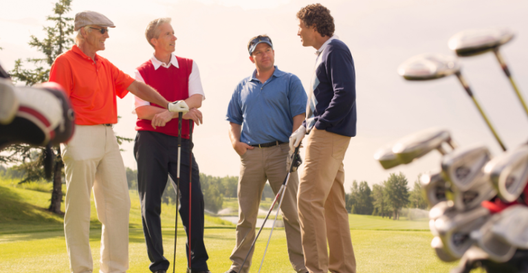 Group of four men chatting on a sunny golf course, standing near their golf clubs.
