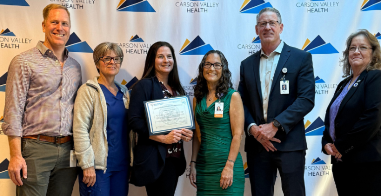 Six Carson Valley Health representatives posing together at a presentation, with one member holding the framed Level IV Trauma Center certification plaque.