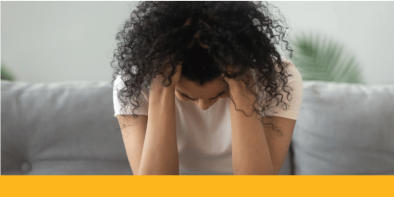 woman looking down at the ground with hands in hair, looking sad